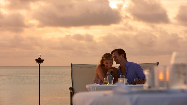 A couple enjoying an intimate moment dining on the beach with sun backlit clouds in the background.