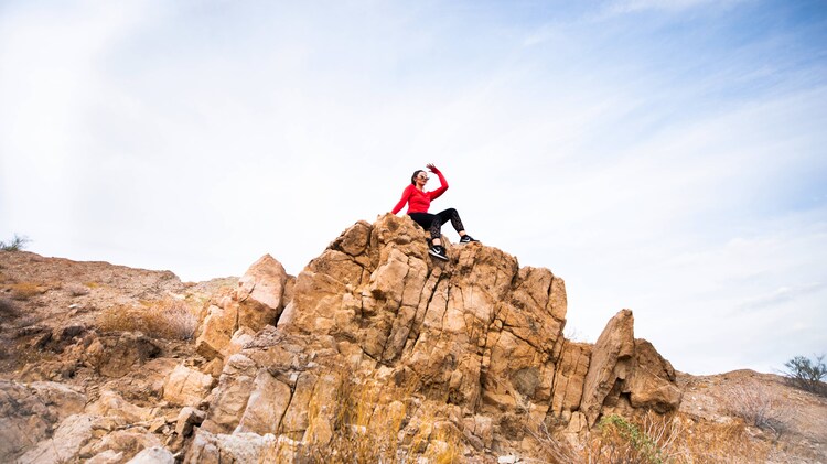 A woman sitting atop a rocky outcropping near a hiking trail.