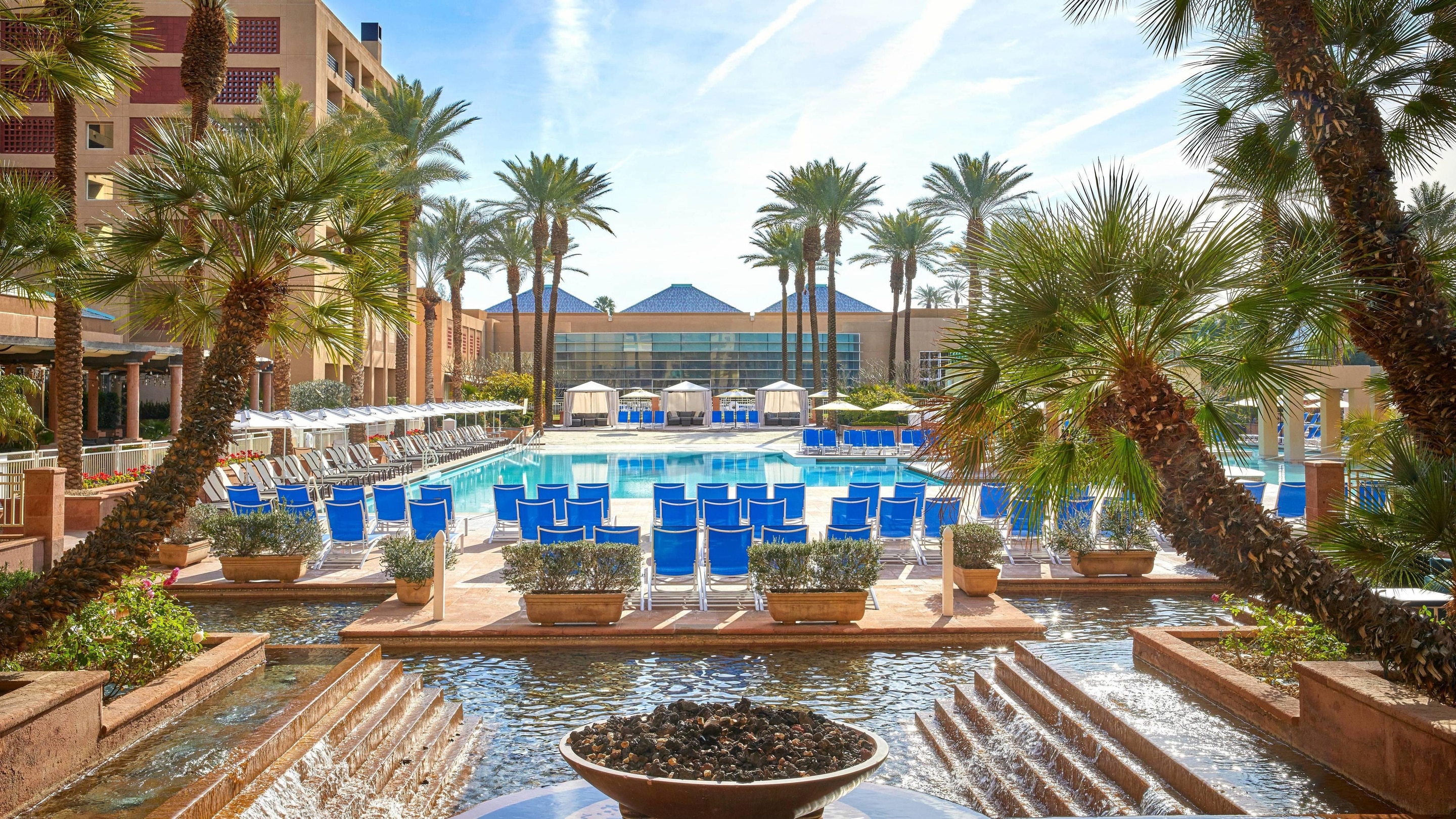 An expansive outdoor pool surrounded by palm trees and blue fabric chairs.