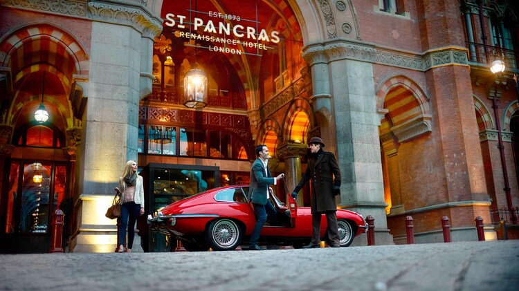 Man and woman exiting a vintage red car at the St. Pancras Hotel entrance.