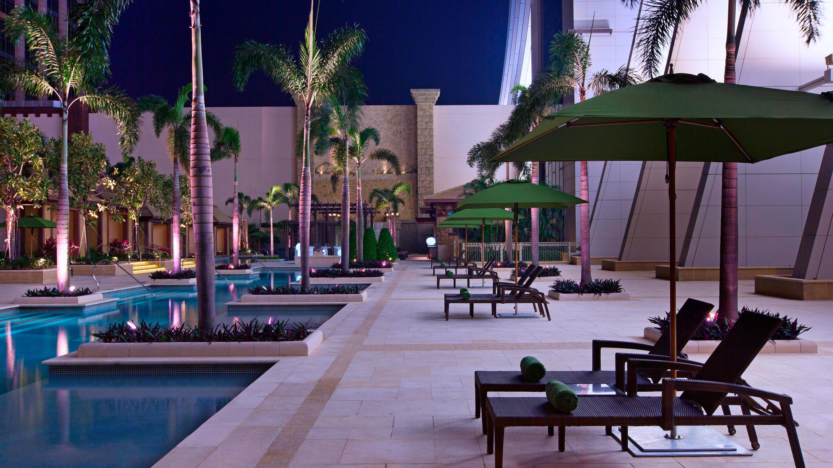 Poolside lounges in the evening next to lighted pool and palm trees