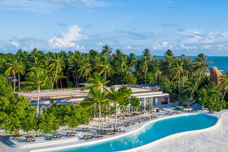 Exterior of st. regis maldives resort with main swimming pool among the palm trees.
