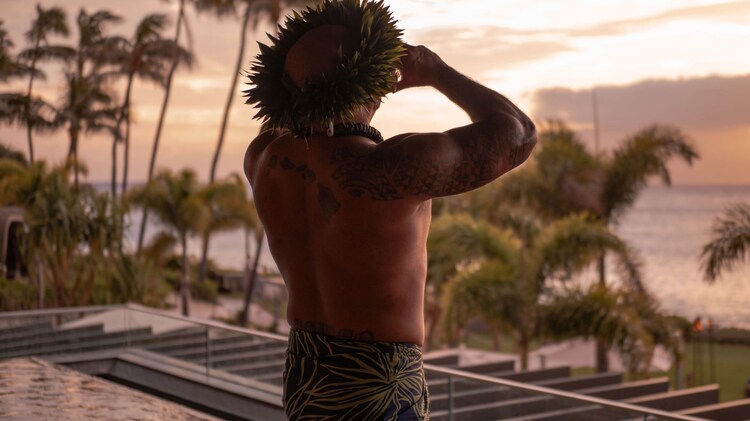 Man with leaves on his head looks into sunset.