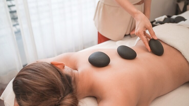 Person on massage table with small stones up and down their back. 