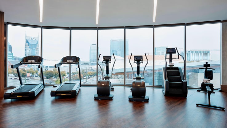 Fitness machines facing a large panoramic bank of windows overlooking the city.