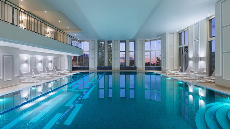 Expansive indoor pool with floor-to-ceiling windows on one side of the room, and a balcony overhead. 