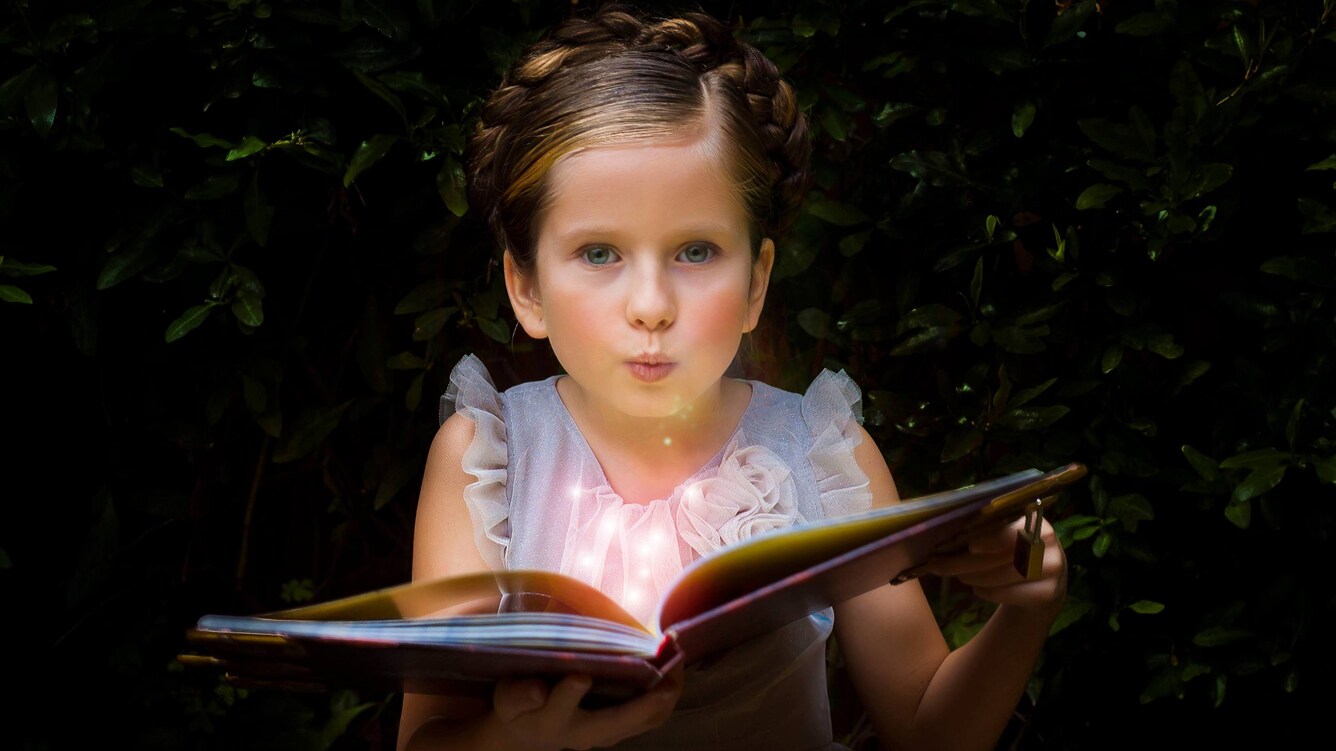 A little girl holding a story book that is lighting up.