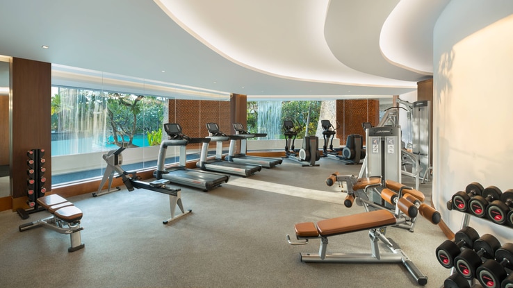 Small gym with floor-to-ceiling windows looking out over resort pools.
