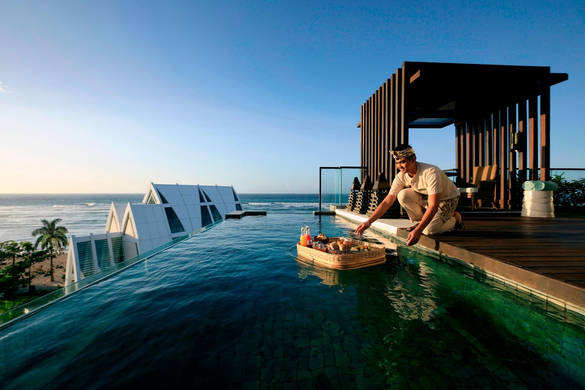 Server setting floating breakfast into a private villa pool.