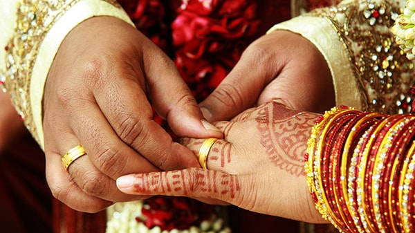 A male hand places a ring on a female hand decorated with henna