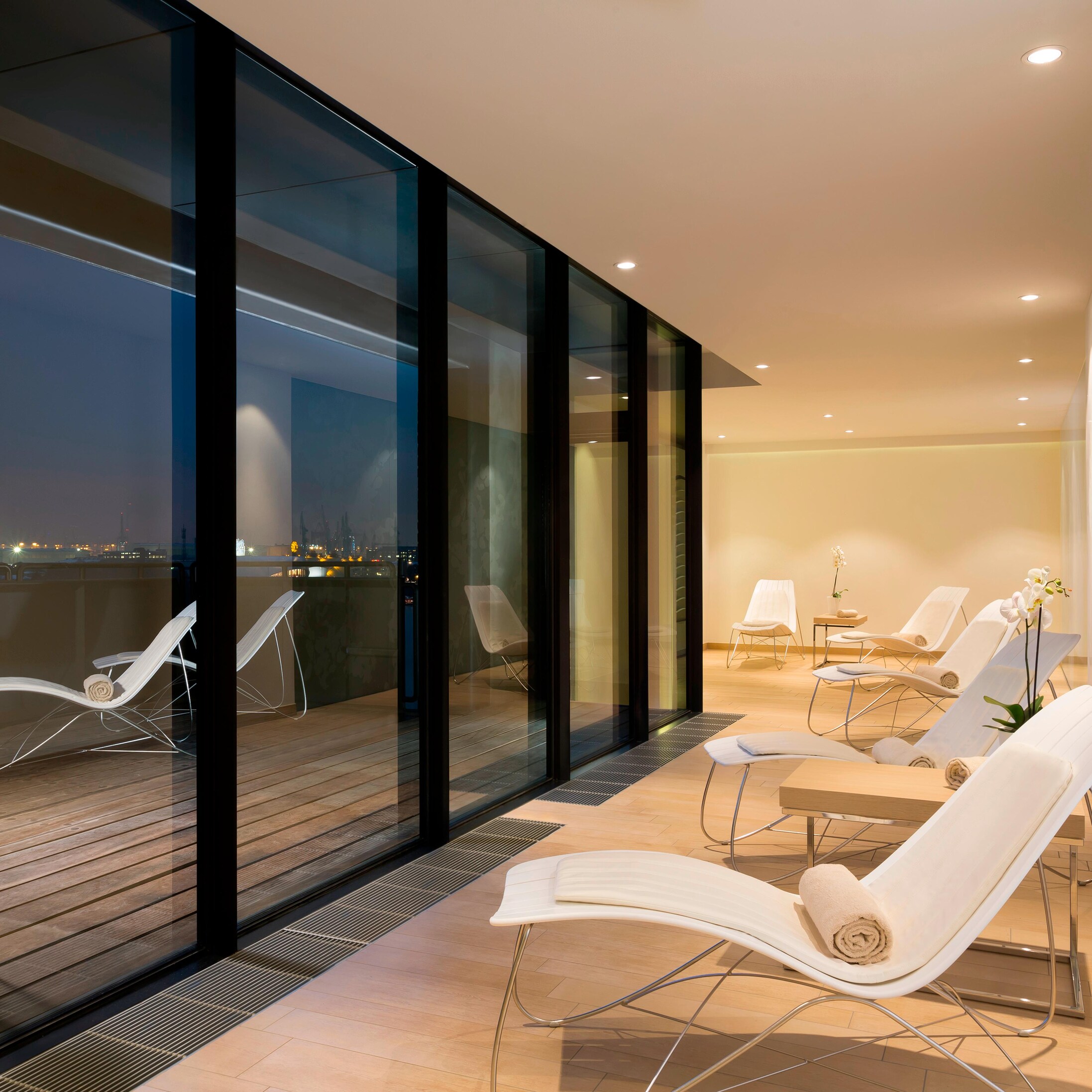 Line of lounge chairs facing floor to ceiling windows at dusk.