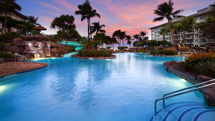 Outdoor hotel pool with sunset and palm trees.