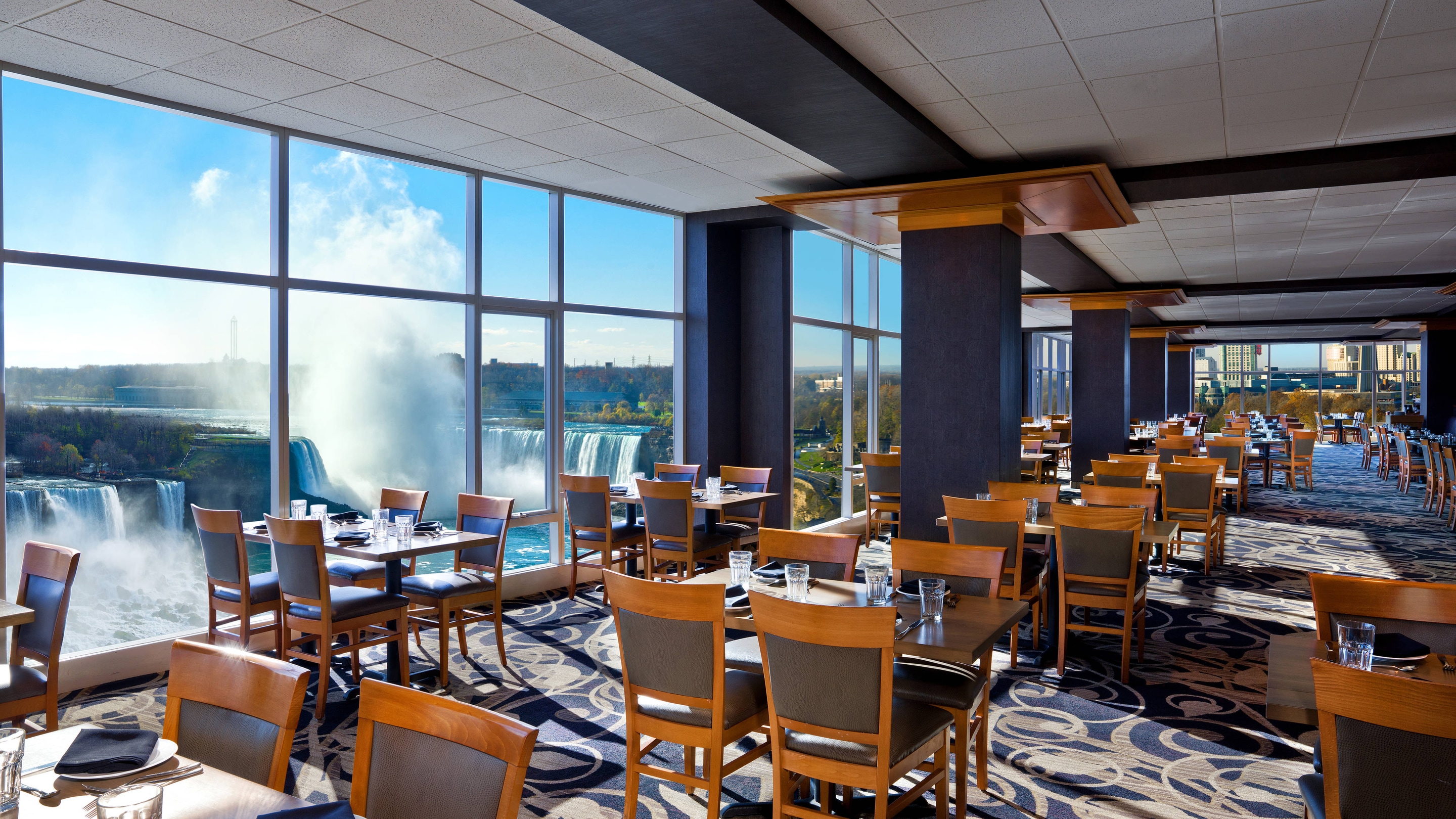 Restaruant with tables and chairs next to windows showing Niagara Falls.