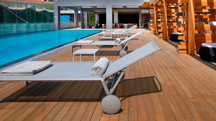 Outdoor pool surrounded by a wooden deck and poolside lounge furniture.