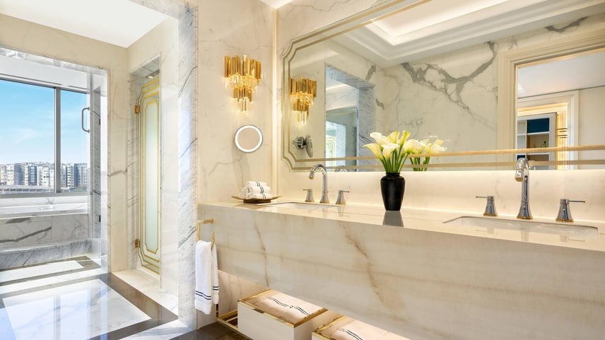 Ritz-Carlton Suite bathroom with twin sinks, walk in shower and a bath tub with a large window next to it.