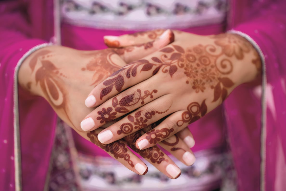 Close up view of the henna tattooed hands of a woman in bright magenta clothing.