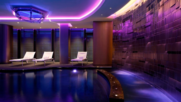 Indoor swimming pool with ambient lighting and poolside lounge chairs.