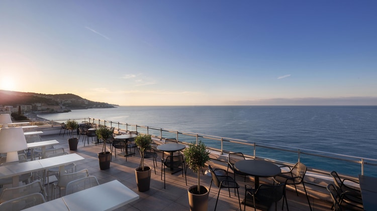 Rooftop restaurant with rows of tables and chairs set overlooking ocean.
