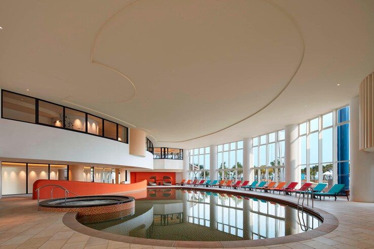 Sheraton okinawa indoor pool with floor to ceiling windows and view of the beach and sea.