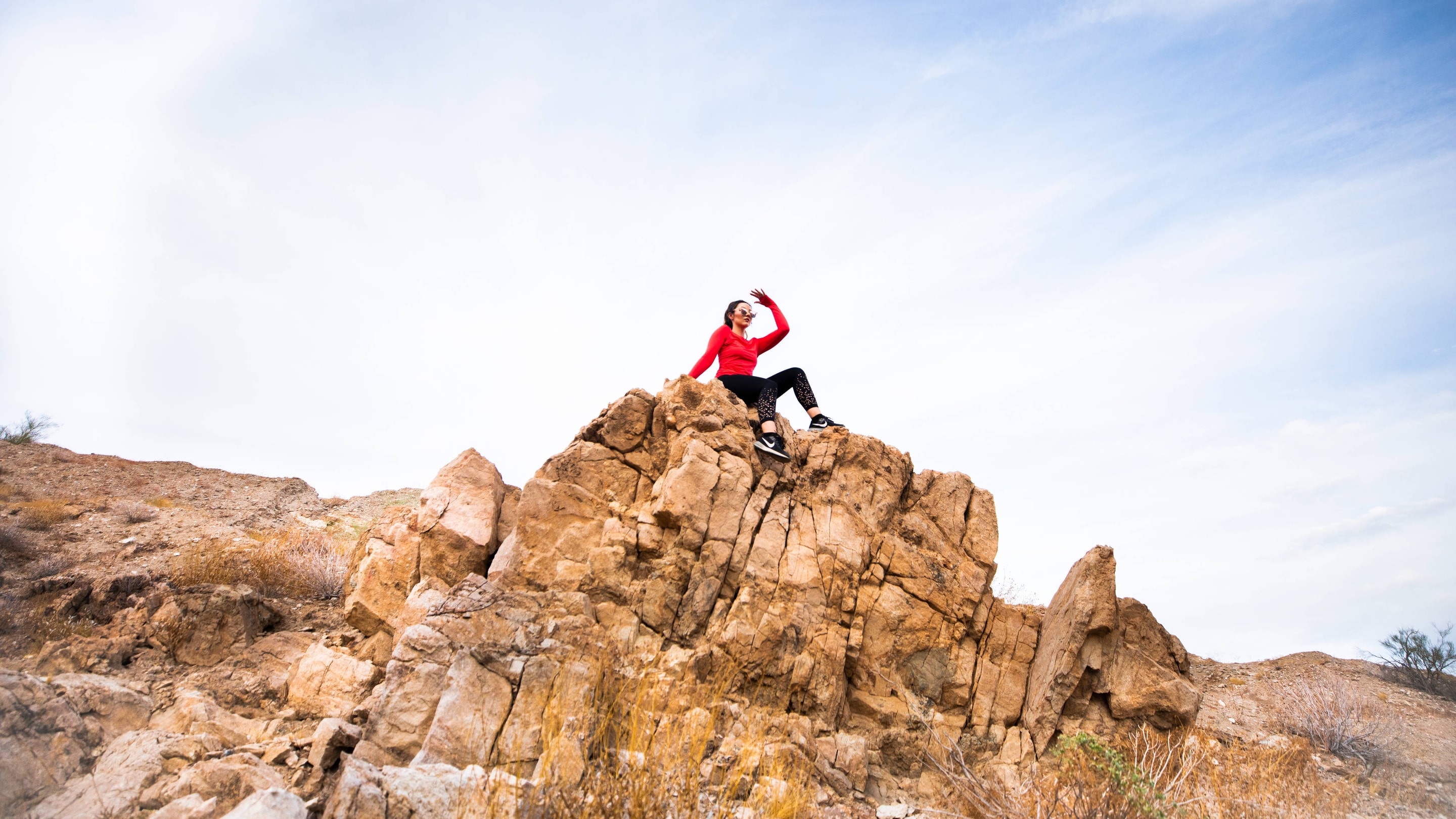 A woman sitting atop a rocky outcropping near a hiking trail.