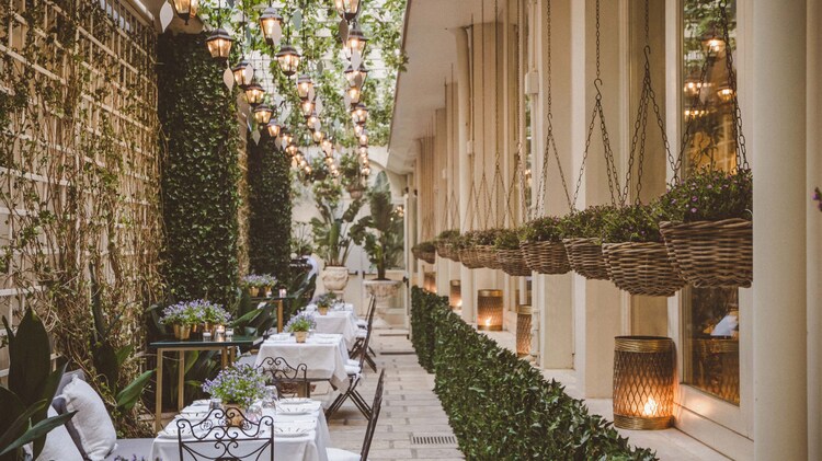 Garden area with row of tables set underneath hanging lights and surrounded by greenery.
