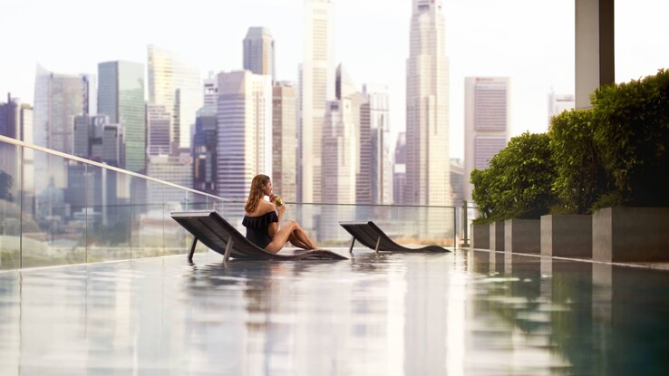 Outdoor pool with woman sitting on chair with view of city