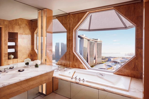 Marble bathroom with a bathtub and an octagonal window overlooking views of Marina Bay