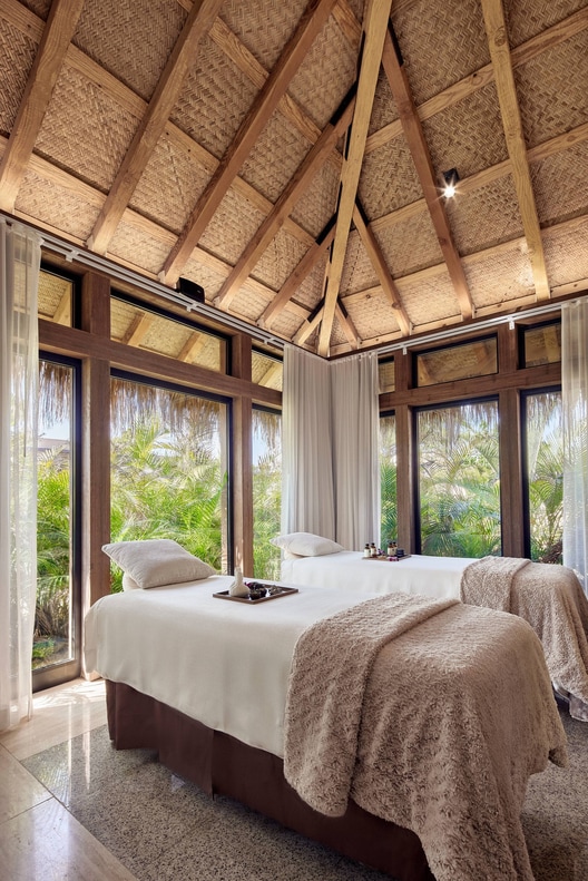 Two massage beds in gazebo with floor to ceiling windows showcasing greenery. 