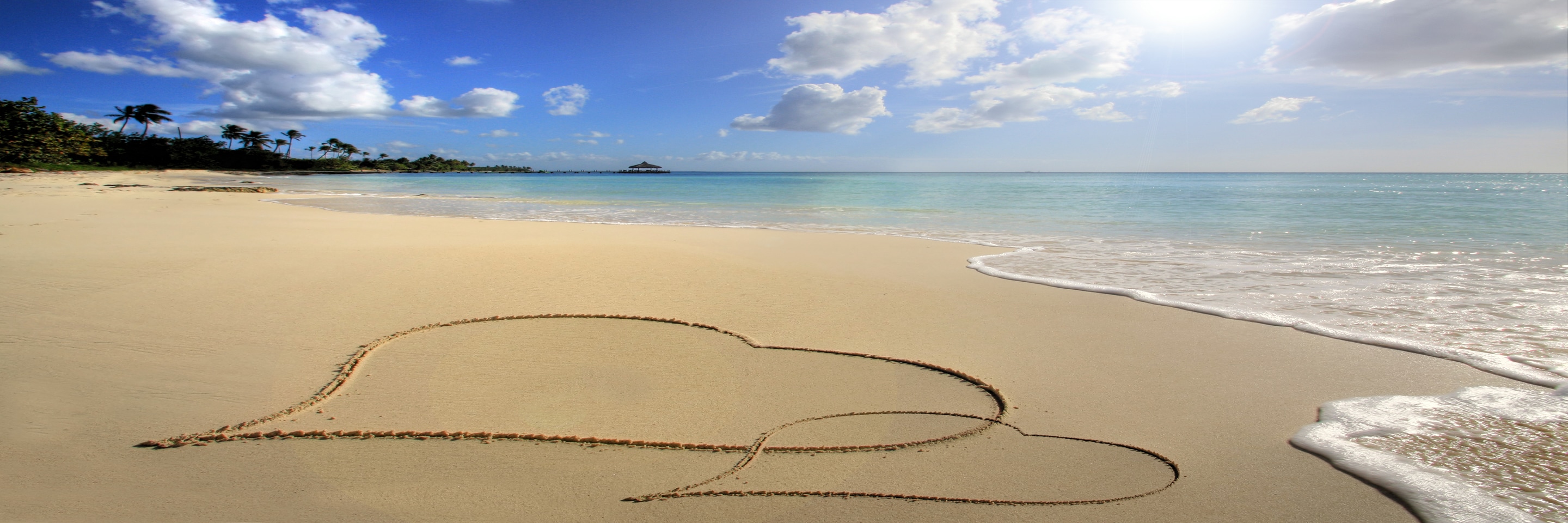 Two hearts drawn in the sand, on a deserted tropical beach with lapping waves.