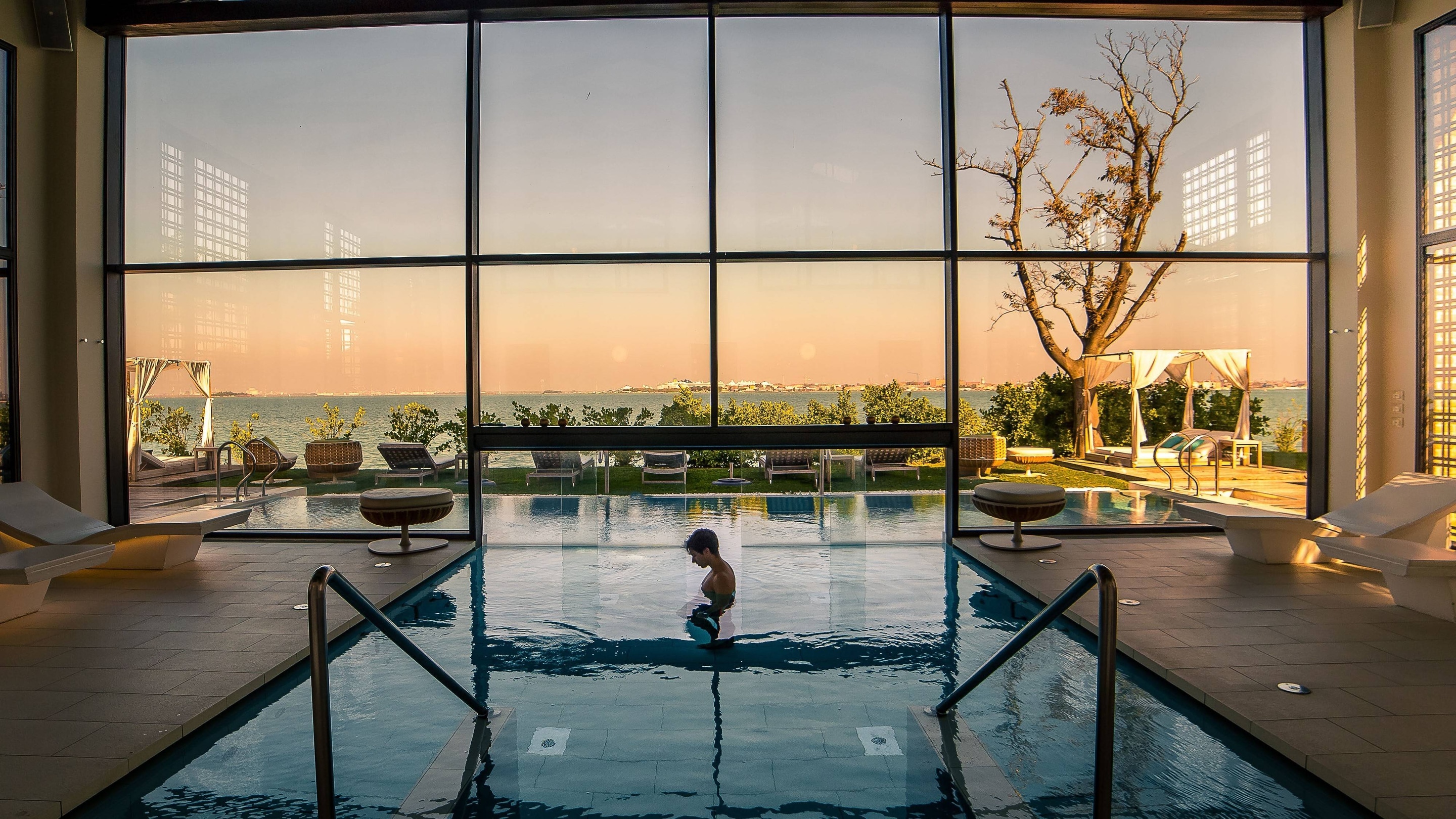Indoor pool with large floor to ceiling windows showing sunset.