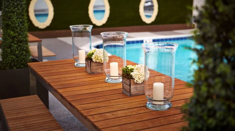 Detail of candles and floral centerpieces on wood table by pool.