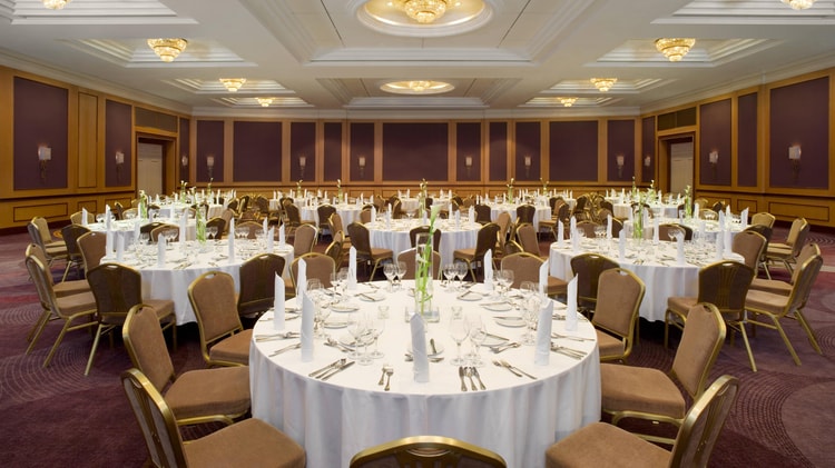 Ballroom set for event with white linens on tables and chairs.