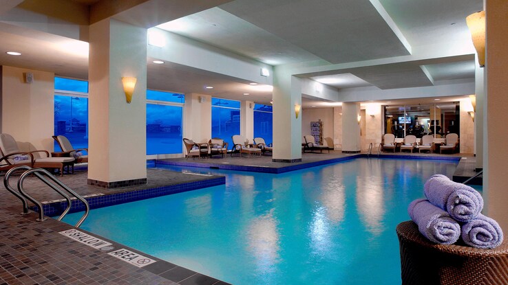 Indoor pool with towels, chaise lounge chairs, and windows