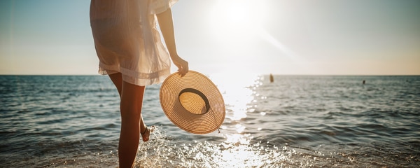Femme tenant le chapeau sur la plage au coucher du soleil d'été