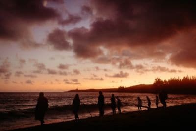 A small group of people stand next to the ocean at sunset.