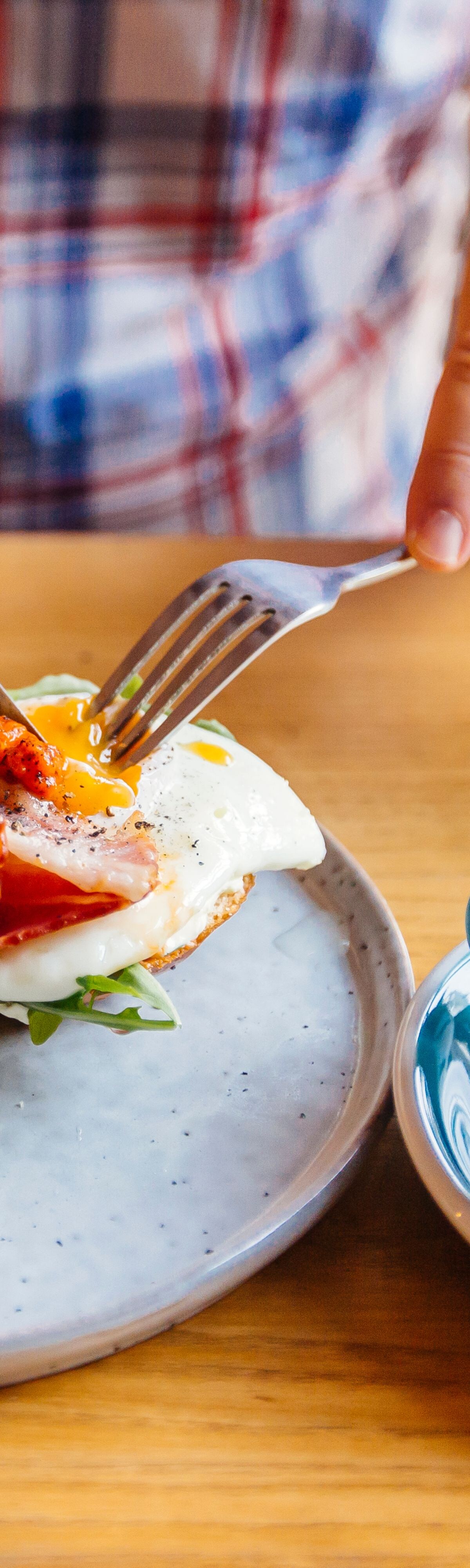 Man eating breakfast with egg, bacon, arugula on brioche bun and coffee