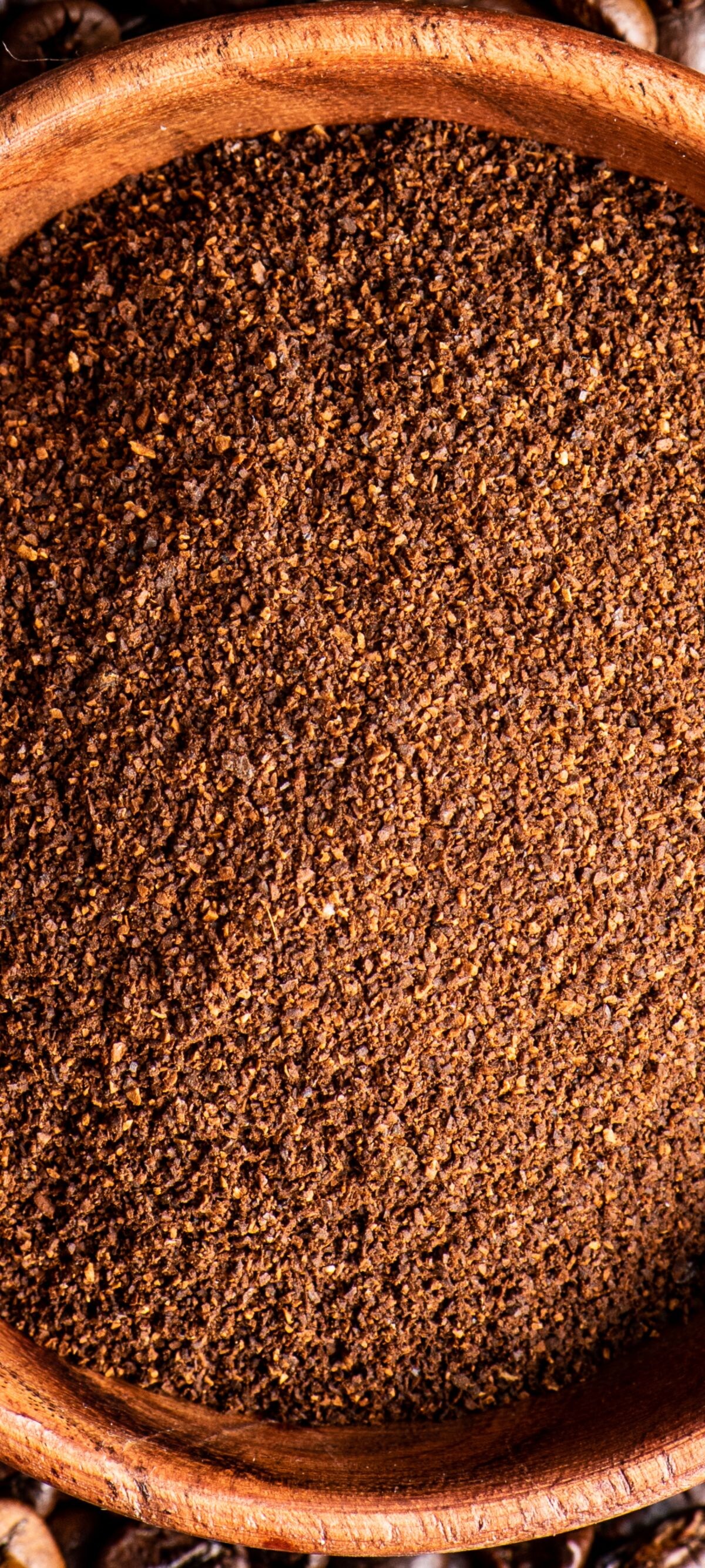 Ground coffee in bowl over coffee beans background