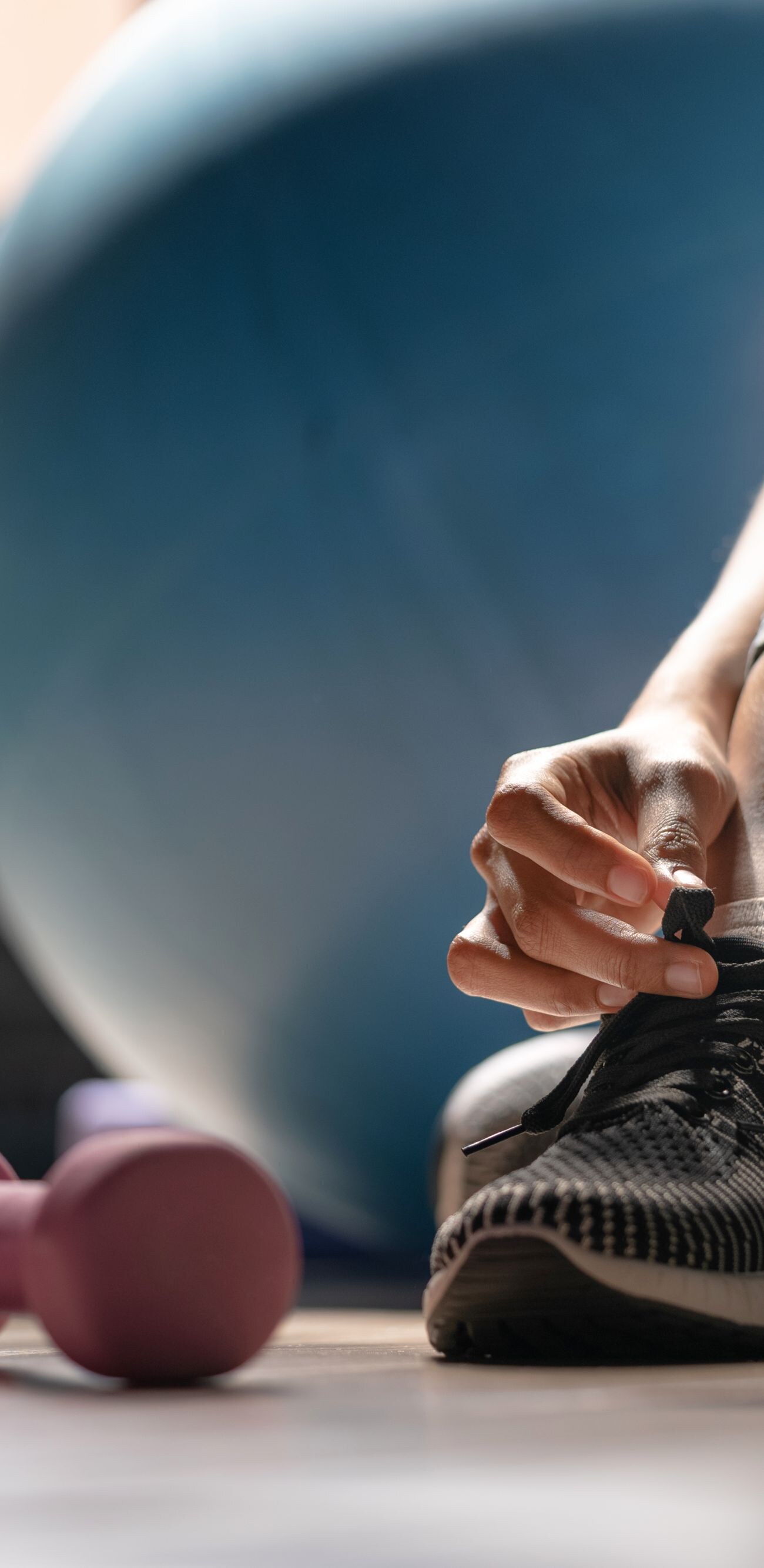 Young sporty woman with smart watch tying shoelaces in fitness
