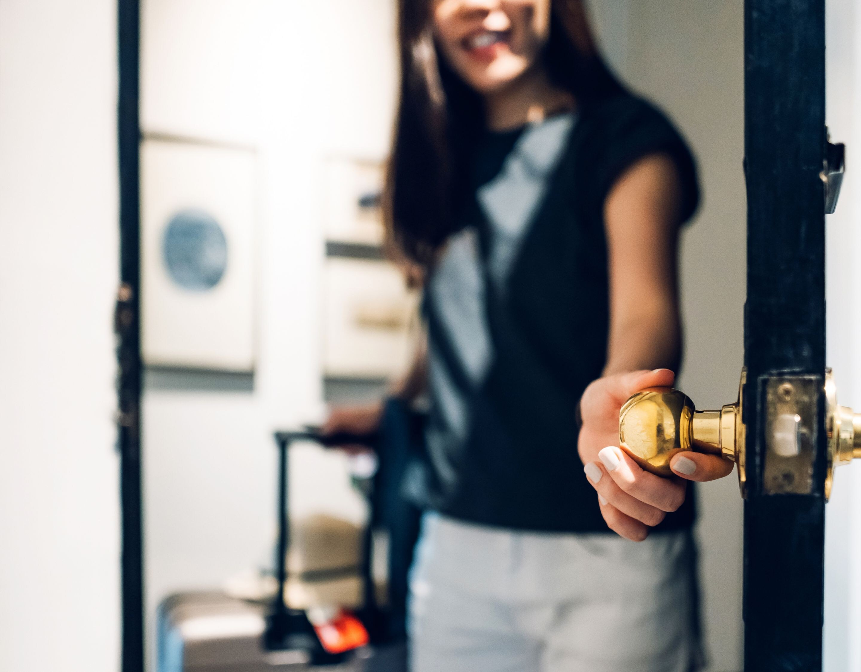 Cheerful young Asian female traveller opening the door entering the hotel room. She is carrying a suitcase and on vacation
