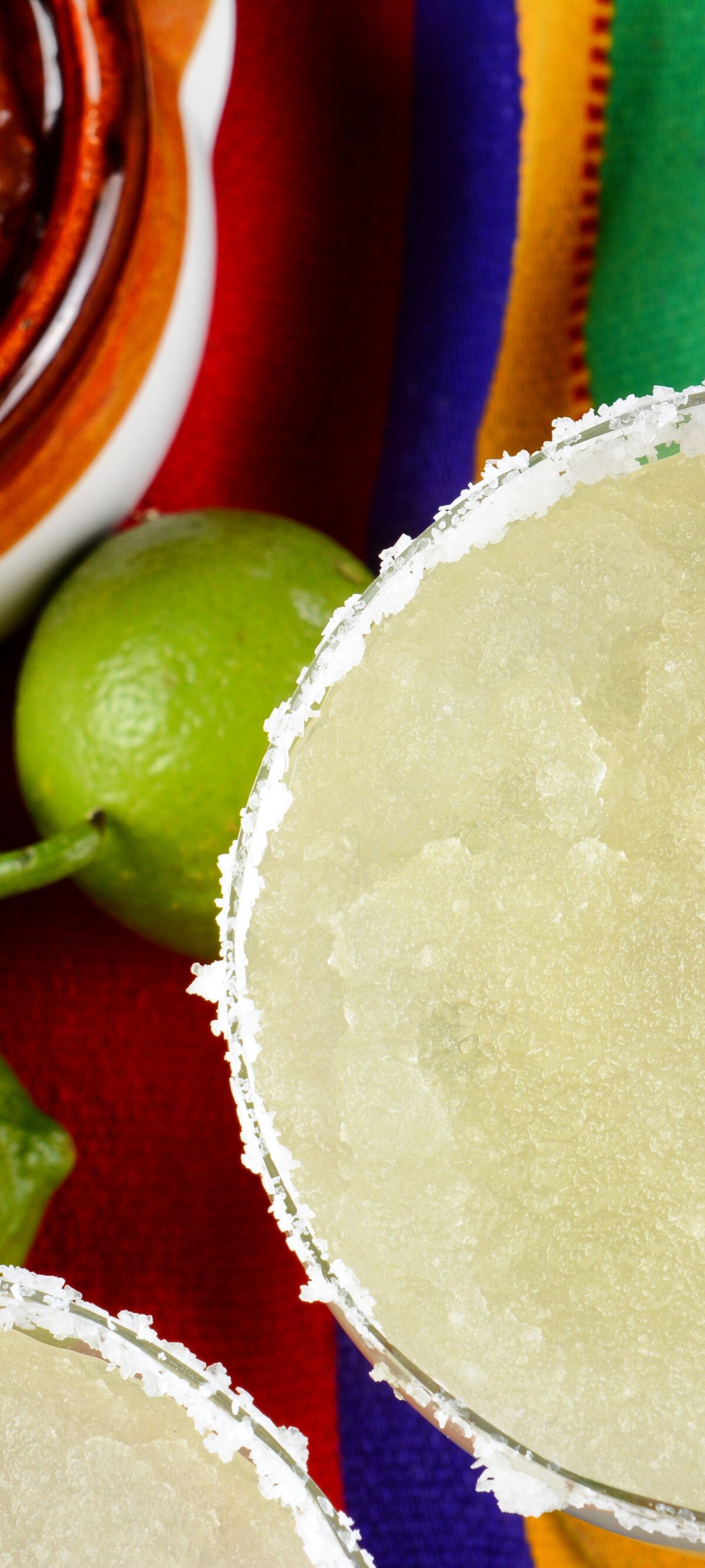 Margaritas and Salsa on a colorful  table cloth, with limes, and peppers.