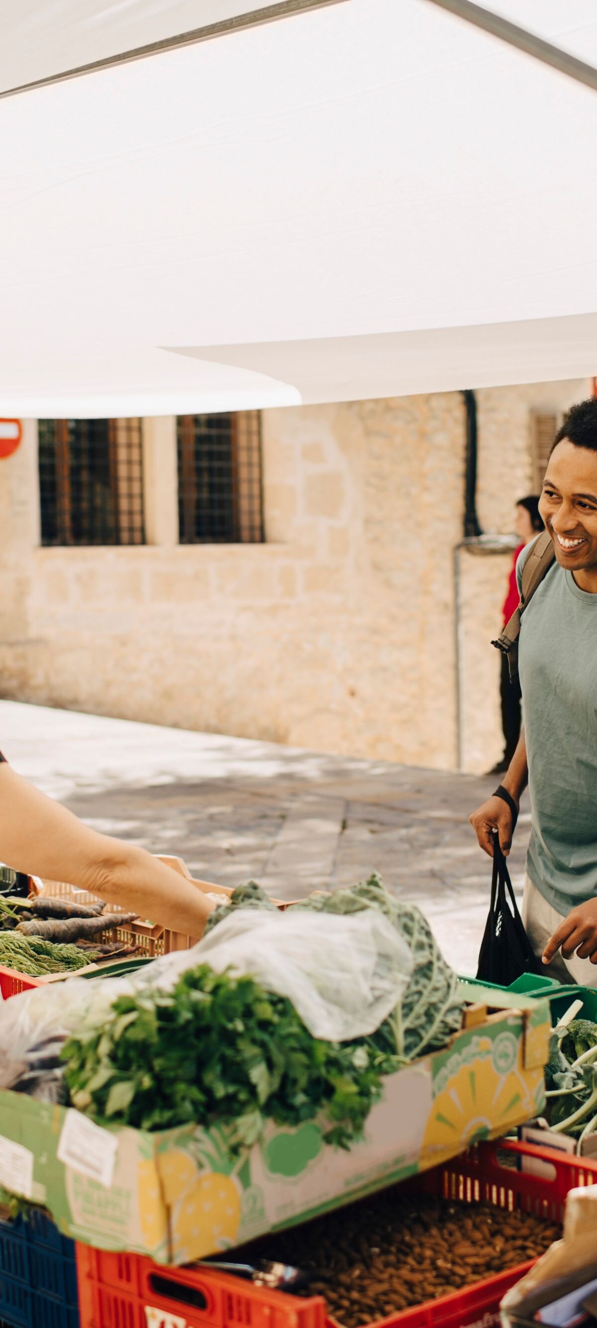Happy male customer buying vegetables from stall in city market on sunny day