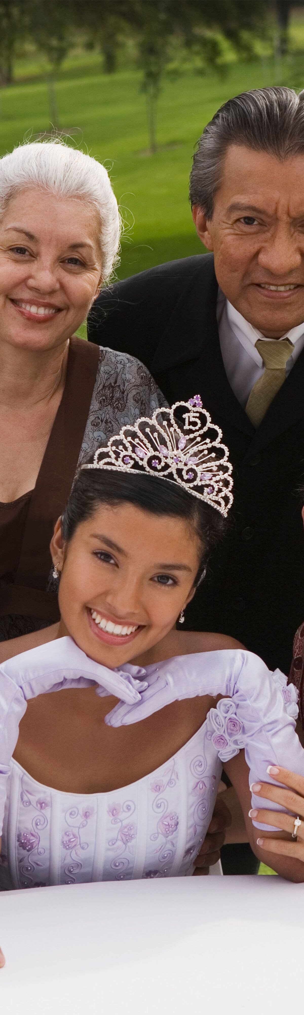 13-15 years, 35-40 years, 40-45 years, 60-65 years years, adults, brunette, celebration, daughter, day, dress, dressed up, eye contact, family, father, formal attire, generations, gown, grandfather, grandmother, grandparents, gray hair, grey hair, half-length, hispanic, latin american, latina, latino, mid-adult man, mid-adult woman, mother, outdoor, parents, portrait, posing, quince anos, quinceanera, senior man, senior woman, small group of people, smile, smiling, suit, teen, teenage girl, teenager, tiara, together, togetherness