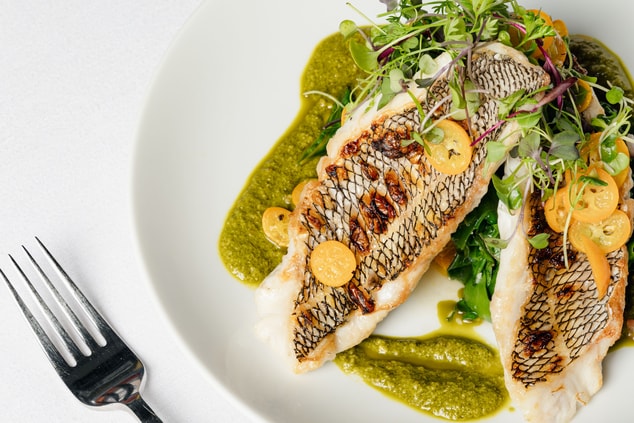 Black bass dish with greens on top of pesto