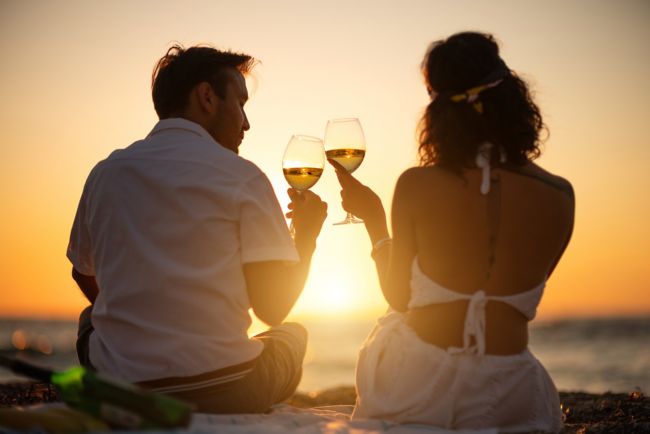 a couple gazing the sunset by the sea sipping wine
