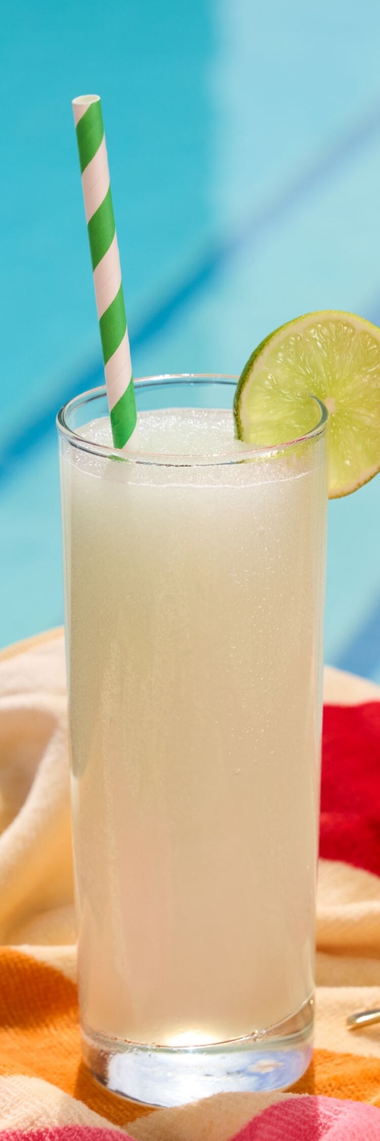 Cocktail in tall glass with green and white straw.