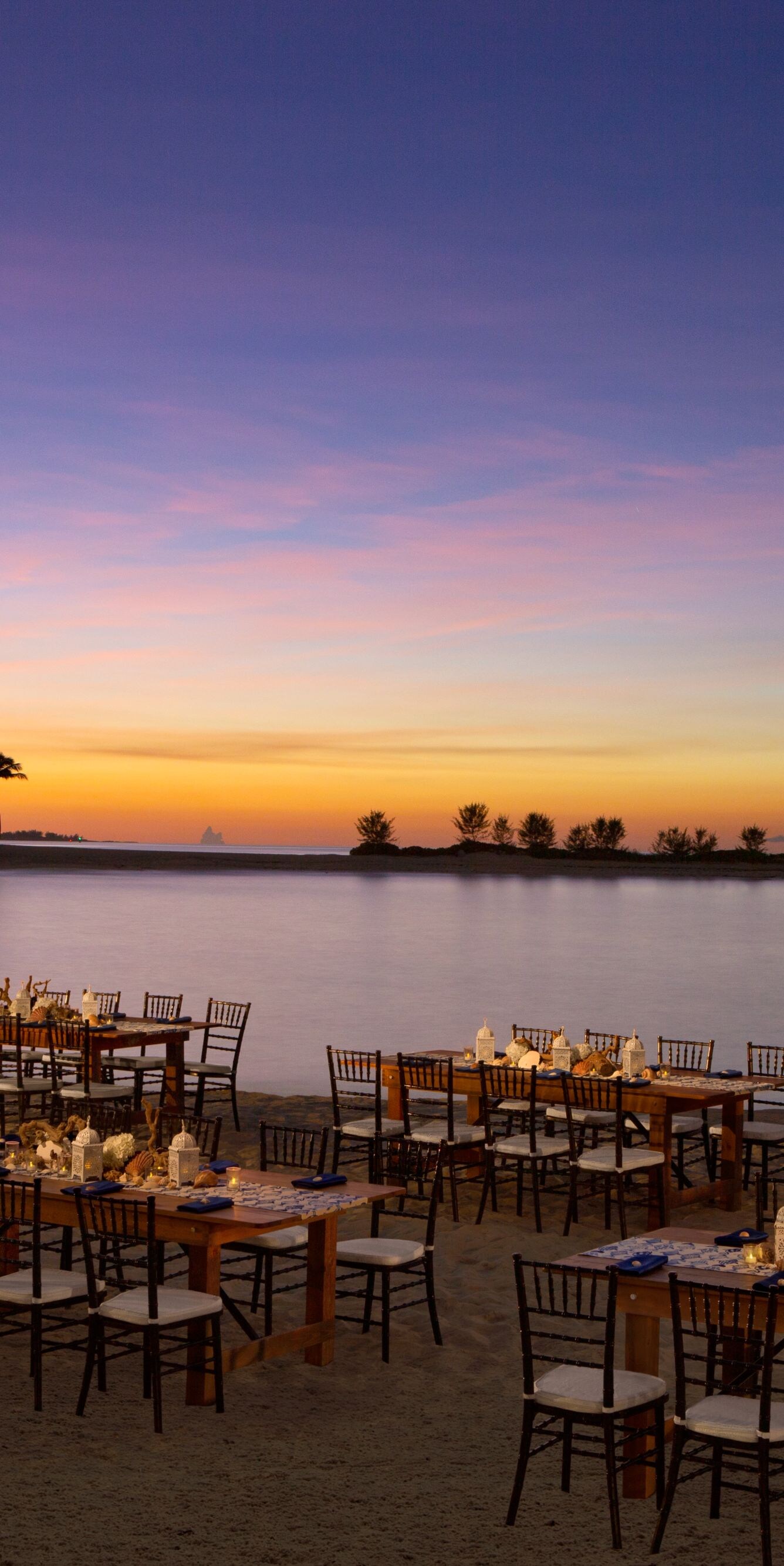 Outdoor tables set along a calm waterfront at dusk