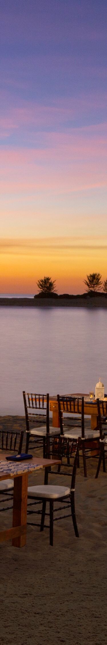 Outdoor tables set along a calm waterfront at dusk
