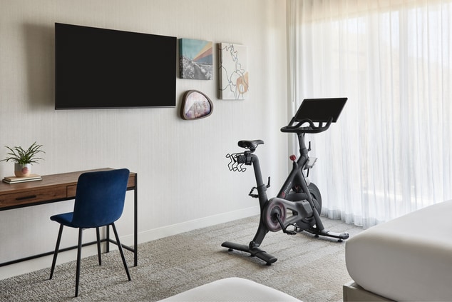 room with Peloton bike, TV, desk, chair