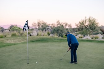 Man putting golf ball at hole