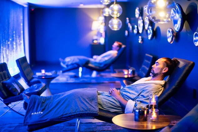 2 men in blue-lit room relaxing on chaise lounges